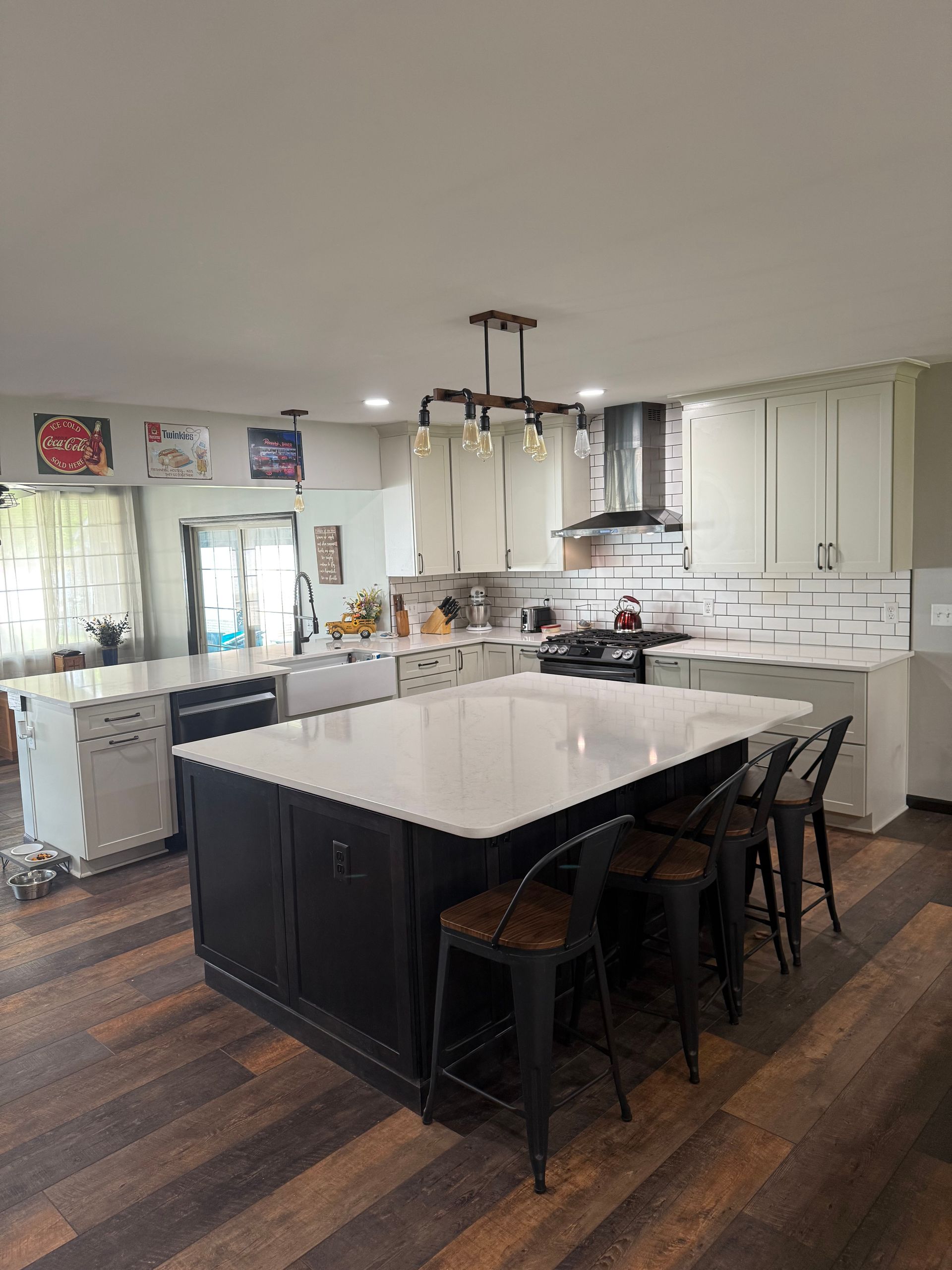 Kitchen with a large black island, white countertops, and bar stools. White cabinets, black range hood.