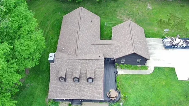 Overhead view of a house with a brown roof and a black deck surrounded by green grass and trees.