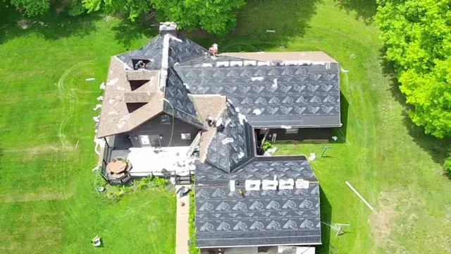 Aerial view of a dark-roofed house surrounded by green grass and trees.