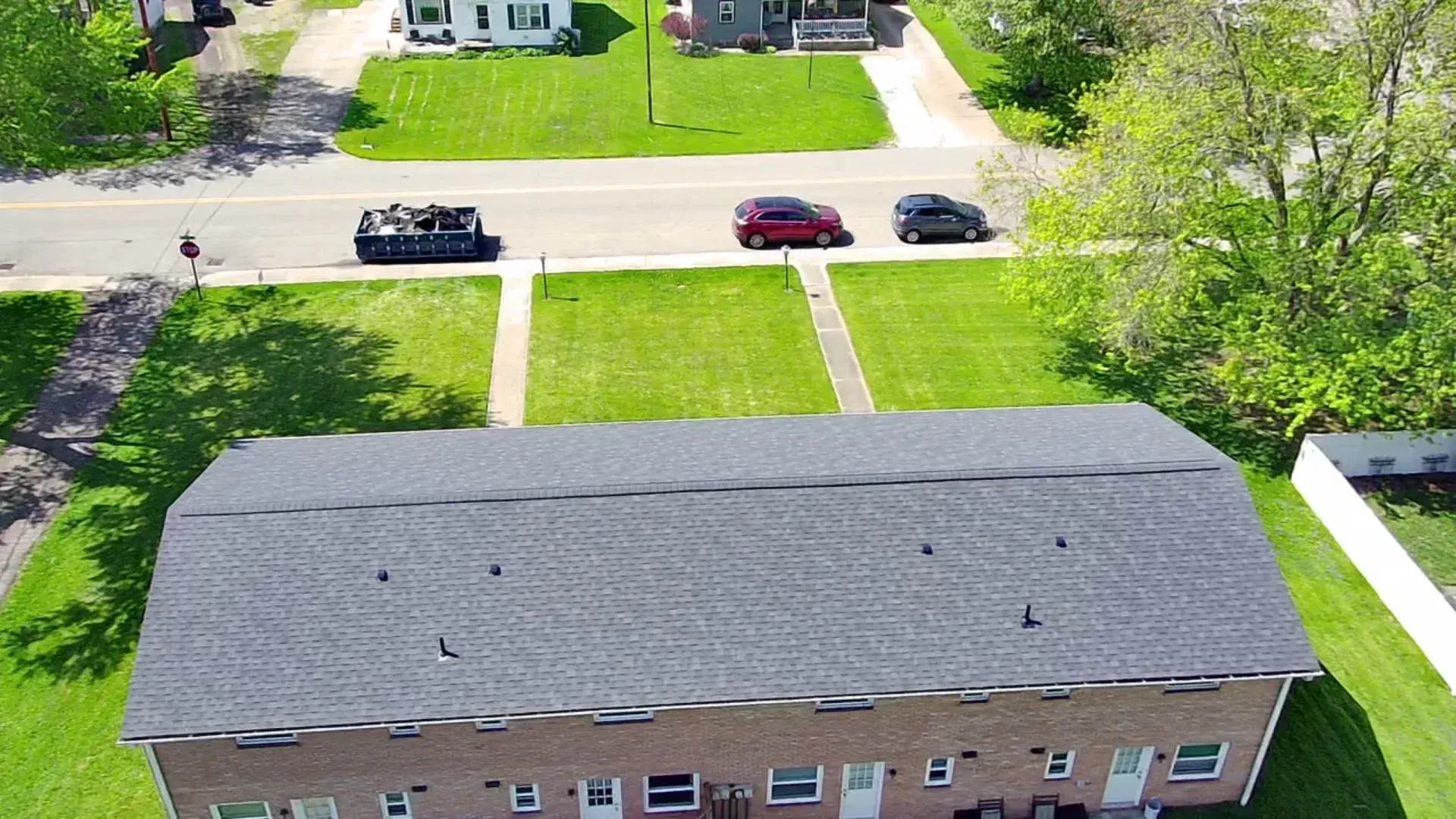Aerial view of a street with a tank, two cars, and houses with green lawns.