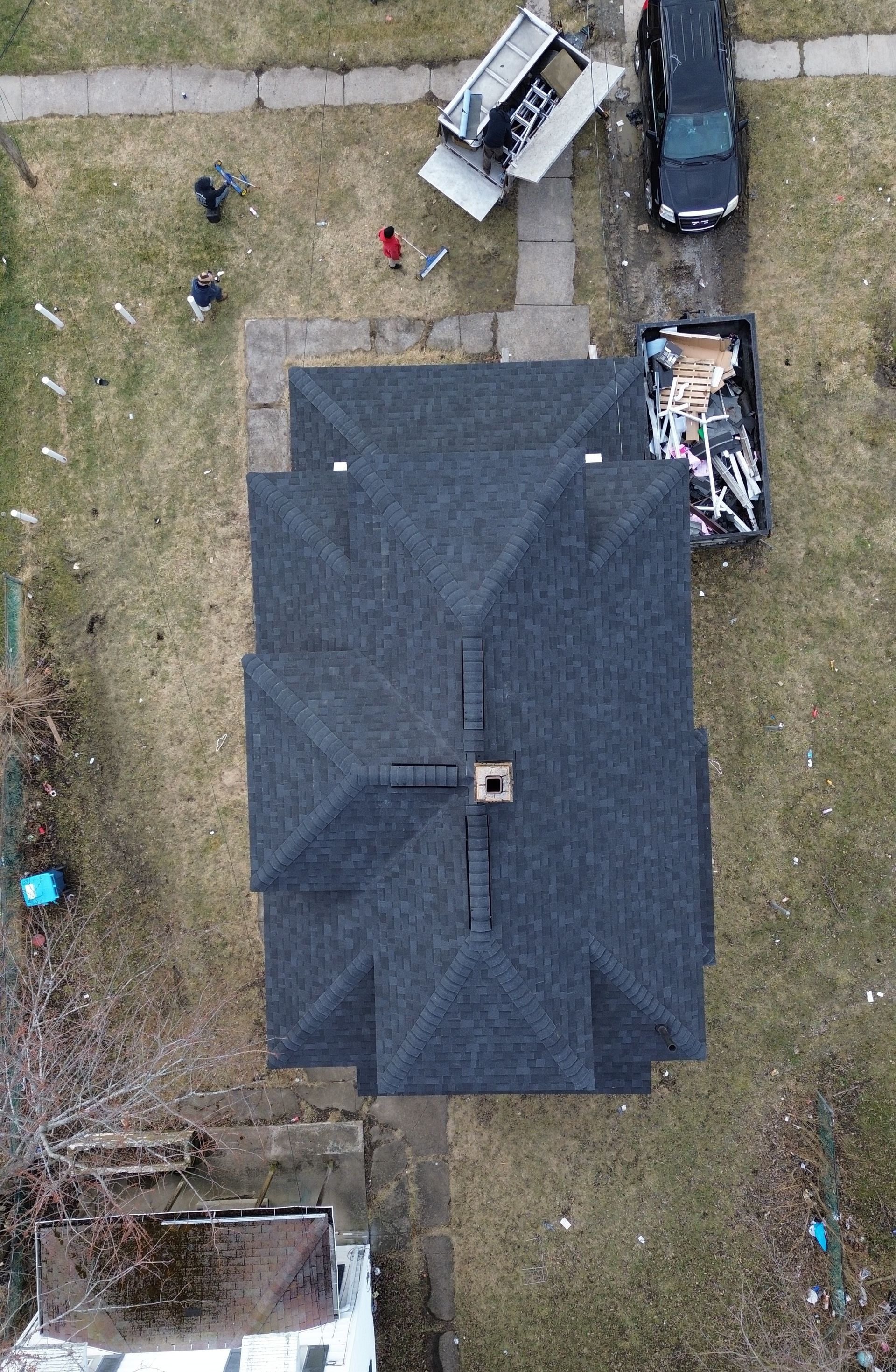 Overhead view of a dark-roofed house with vehicles and debris in the yard.
