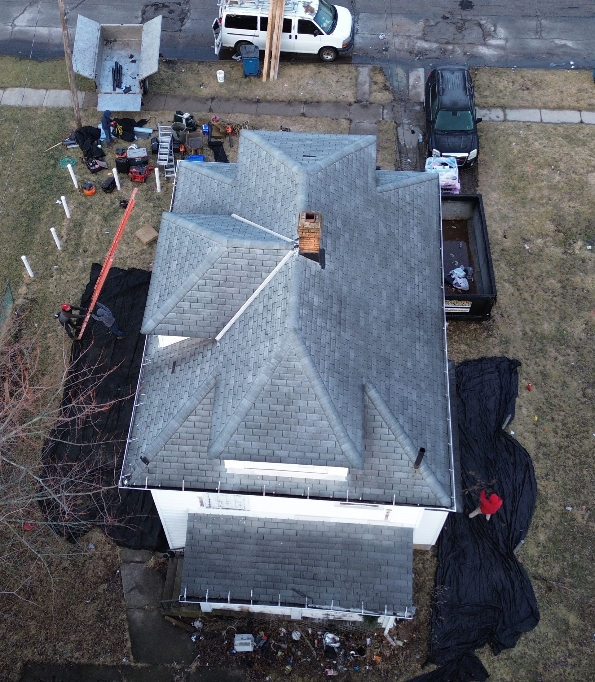 Overhead view of a house with a gray roof, construction equipment, and vehicles in the yard.