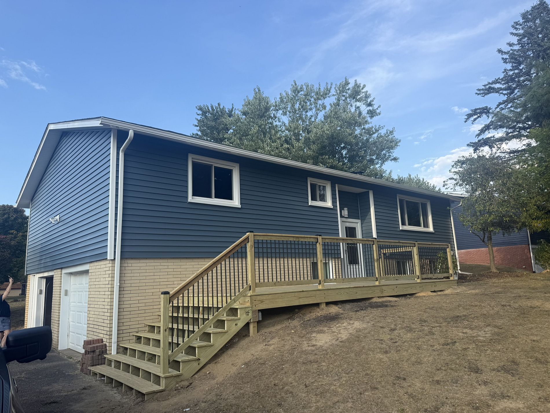 A two-story house with blue siding, a wooden deck, and a set of stairs leading to the entrance.