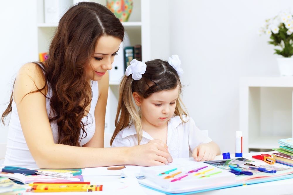 A Woman is Helping a Little Girl With Her Homework — Grandma Rosie’s Quality Long Day Care In Primbee, NSW