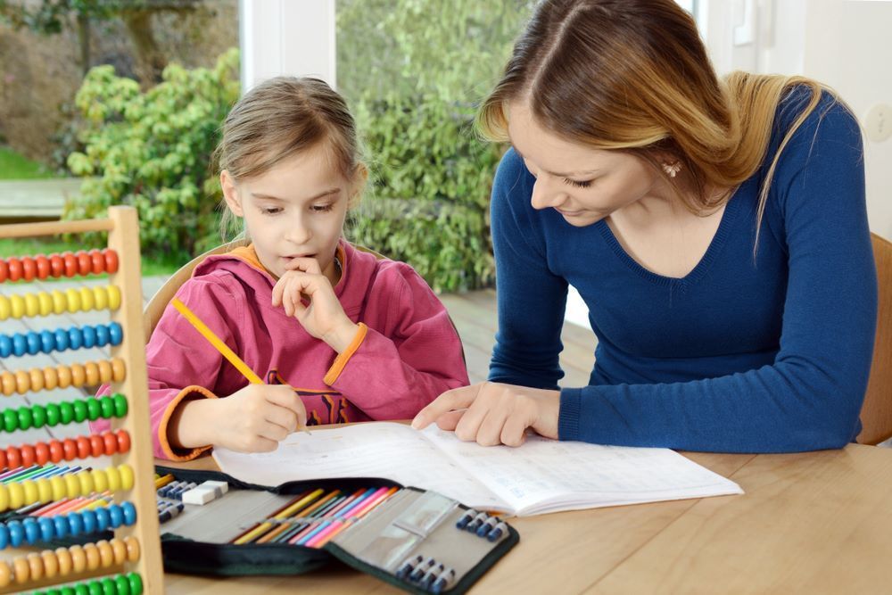 A Woman is Helping a Little Girl With Her Homework — Grandma Rosie’s Quality Long Day Care In Primbee, NSW