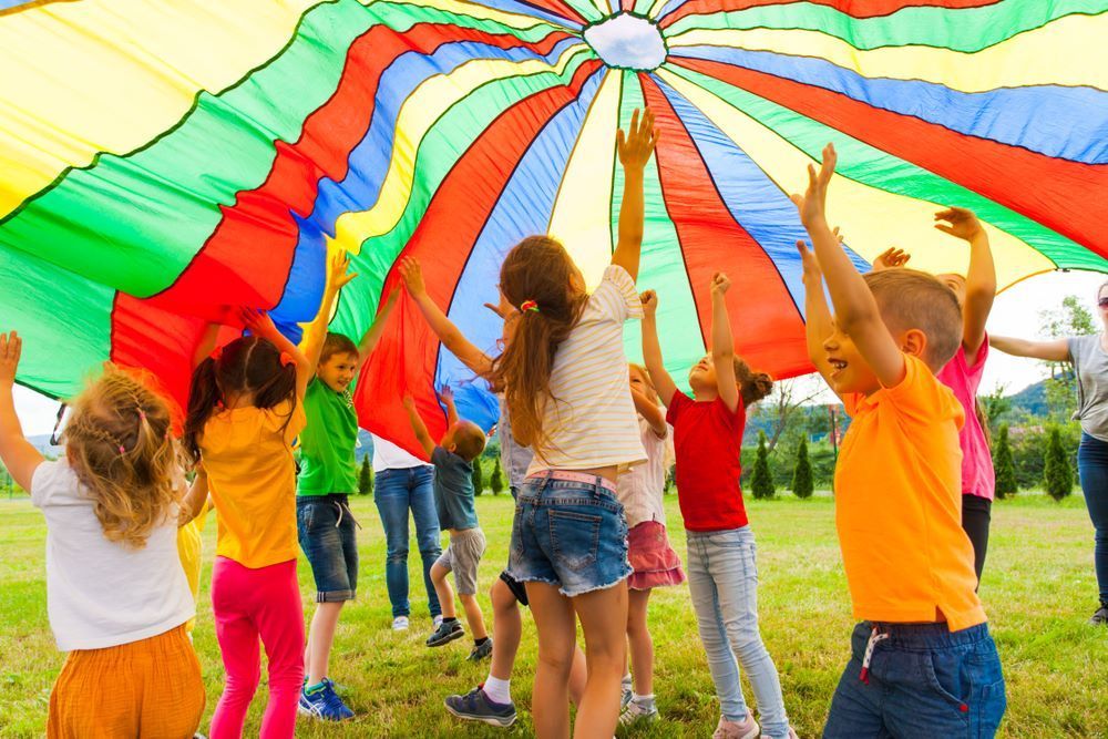 A Group of Children Are Playing Under a Colorful Parachute — Grandma Rosie’s Quality Long Day Care In Dapto, NSW