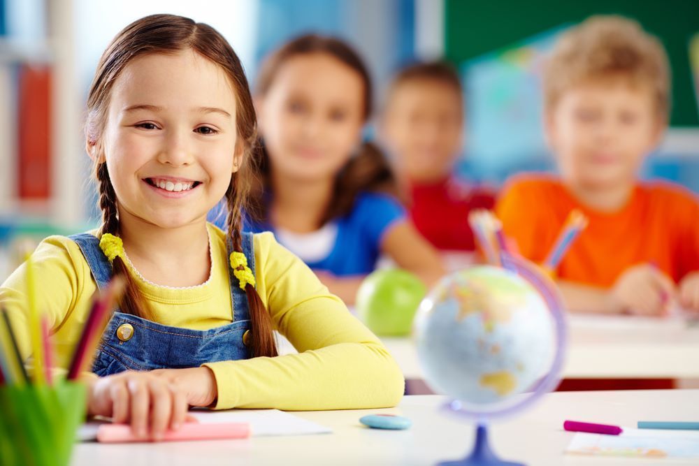 A Young Girl is Sitting at a Desk in a Classroom With Other Children — Grandma Rosie’s Quality Long Day Care In Dapto, NSW
