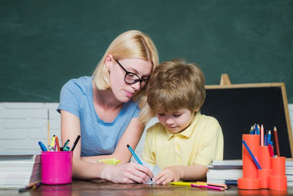A woman is helping a young boy with his homework in a classroom — Grandma Rosie’s Quality Long Day Care In Haywards Bay, NSW