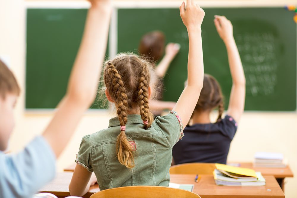 A Group of Children Are Raising Their Hands in a Classroom — Grandma Rosie’s Quality Long Day Care In Dapto, NSW
