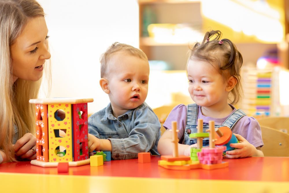 A woman and two children are playing with toys at a table — Grandma Rosie’s Quality Long Day Care In Haywards Bay, NSW