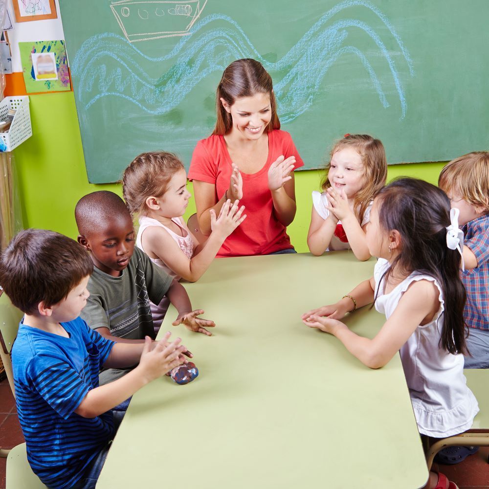 A Group of Children Are Sitting Around a Table With Their Teacher — Grandma Rosie’s Quality Long Day Care In Haywards Bay, NSW