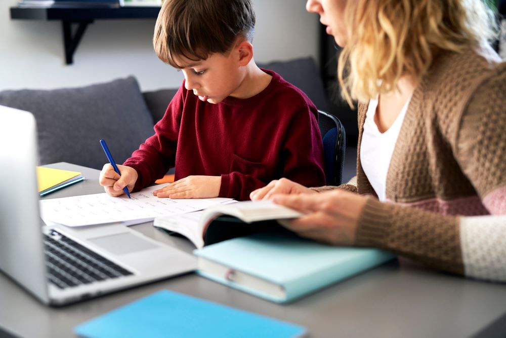 A Woman is Helping a Young Boy With His Homework — Grandma Rosie’s Quality Long Day Care In Haywards Bay, NSW