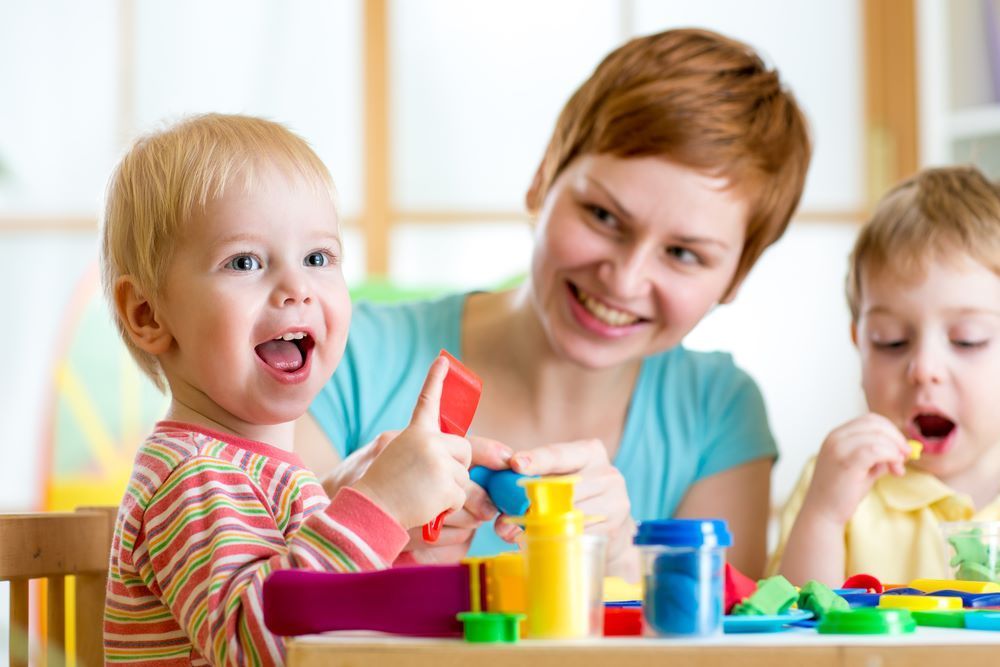 A Woman is Playing With Two Children at a Table — Grandma Rosie’s Quality Long Day Care In Horsley, NSW