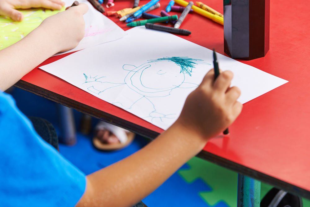Child Drawing Person On Paper With Felt Pen In Kindergarten — Grandma Rosie’s Quality Long Day Care In Wollongong, NSW