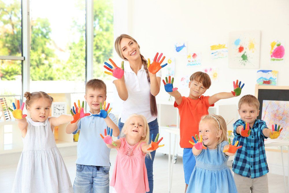Children And Teacher With Hands In Paint At Art Lesson — Grandma Rosie’s Quality Long Day Care In Wollongong, NSW