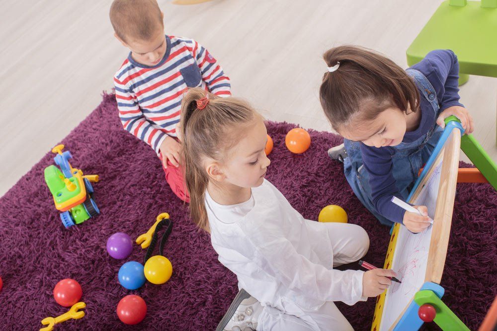One Boy And Two Girls Children Writing On The White Board — Grandma Rosie’s Quality Long Day Care In Wollongong, NSW