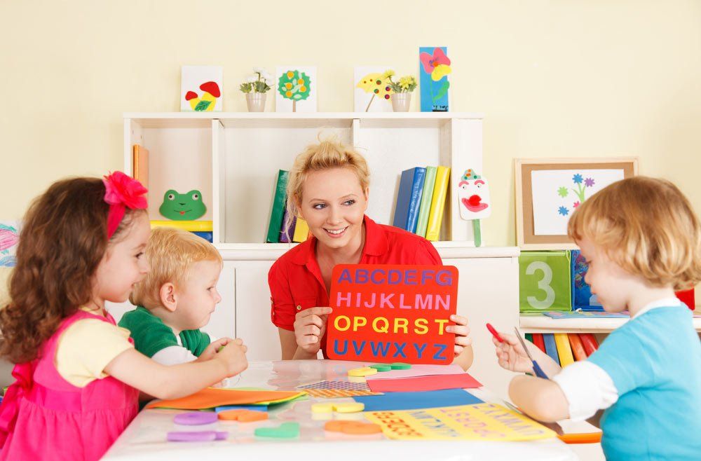 Preschool Teacher Holding The Alphabet With Three Little Children — Grandma Rosie’s Quality Long Day Care In Wollongong, NSW
