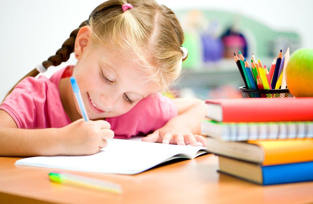 Little Girl Is Writing At The Desk — Grandma Rosie’s Quality Long Day Care In Wollongong, NSW