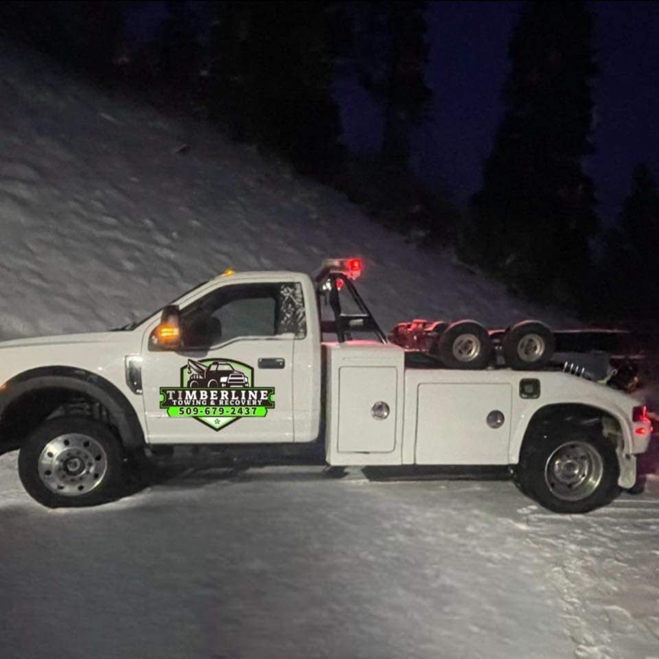 A white tow truck is parked in the snow at night.