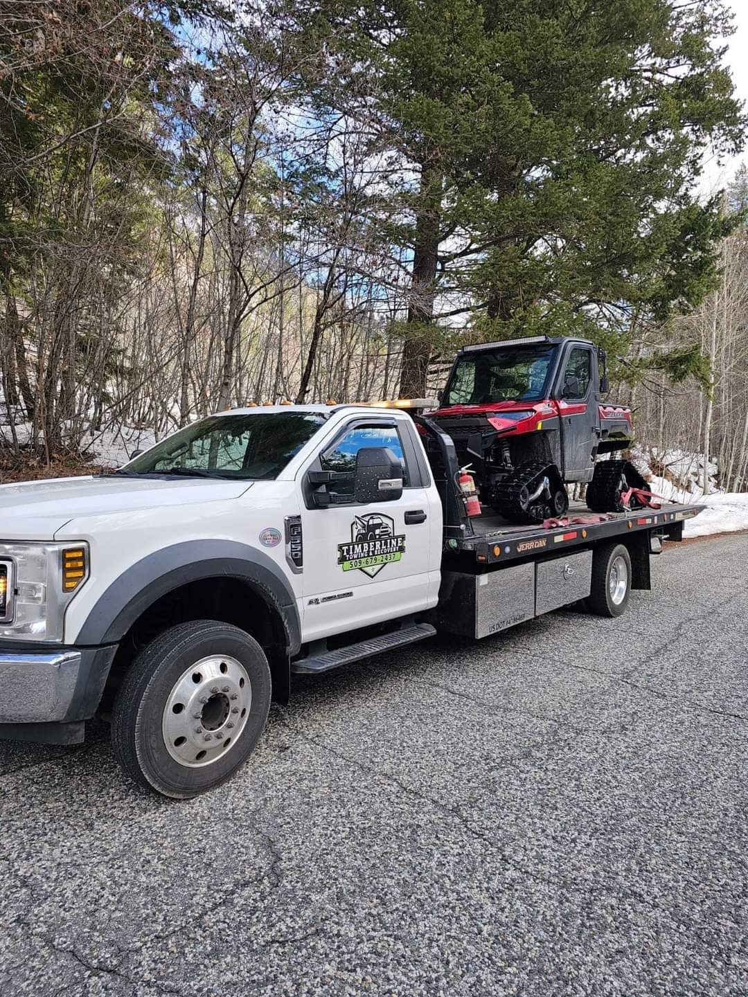 A white tow truck is towing a red atv on a gravel road.