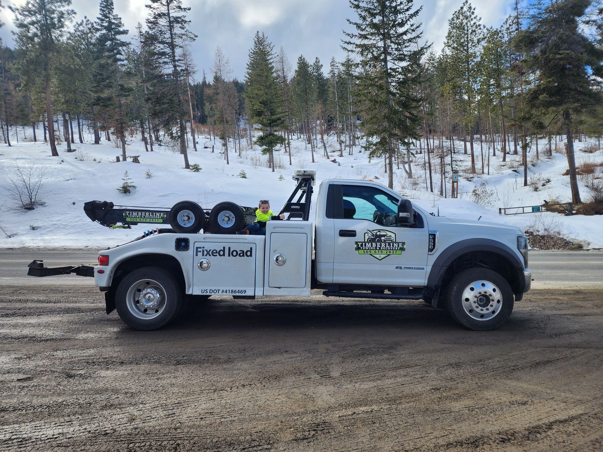 A white tow truck is parked on the side of the road in the snow.
