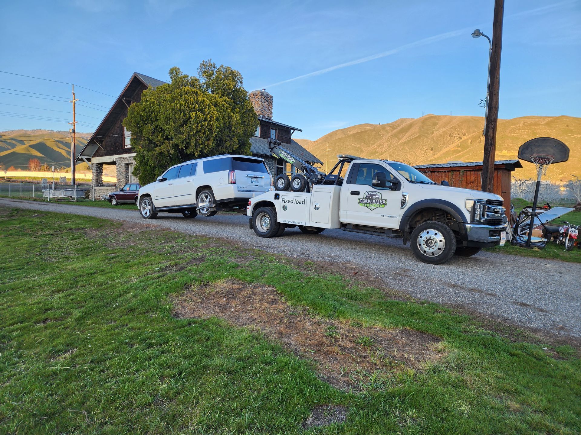 A white tow truck is towing a white suv on a gravel road.