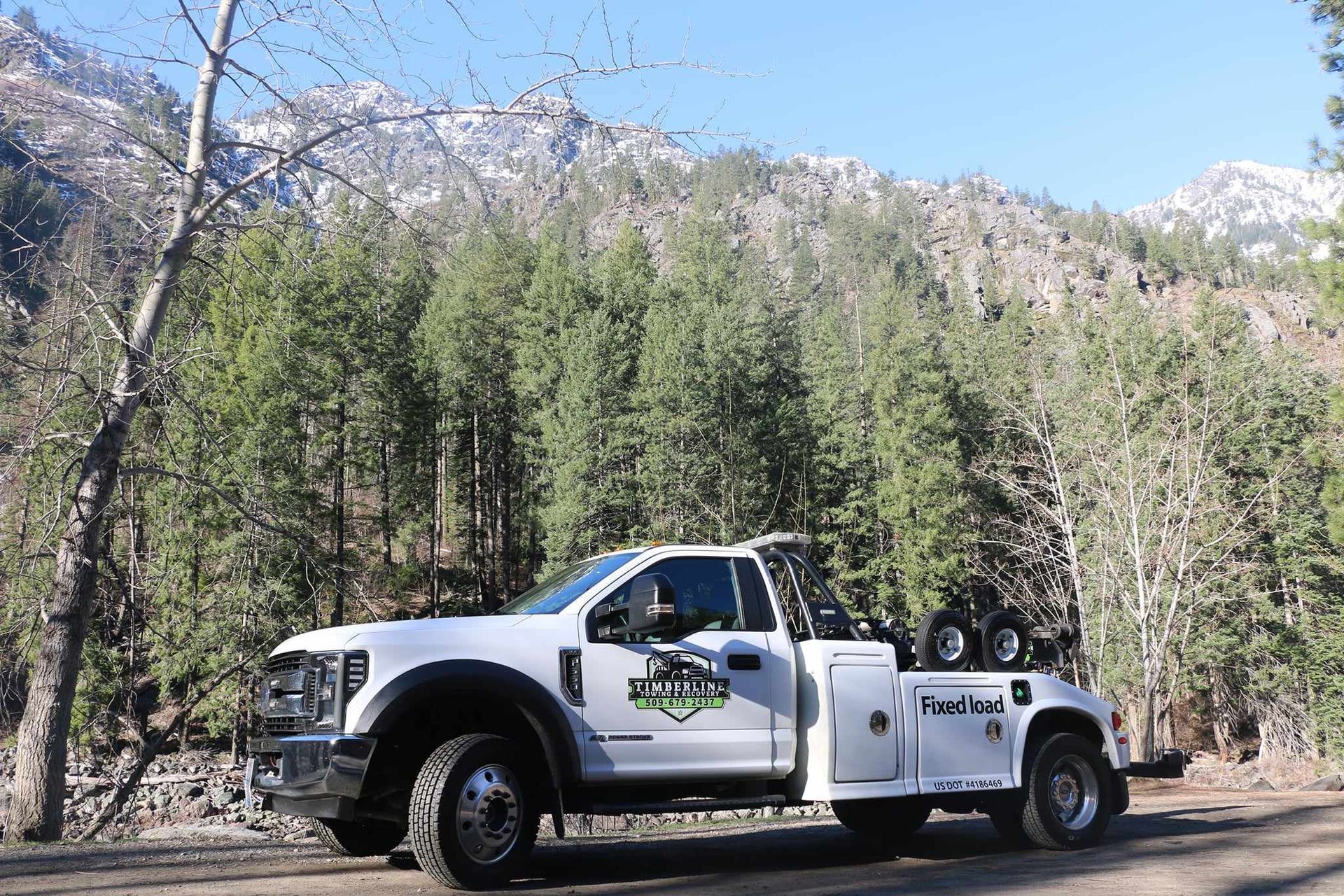 A white tow truck is parked on the side of a road in the woods.