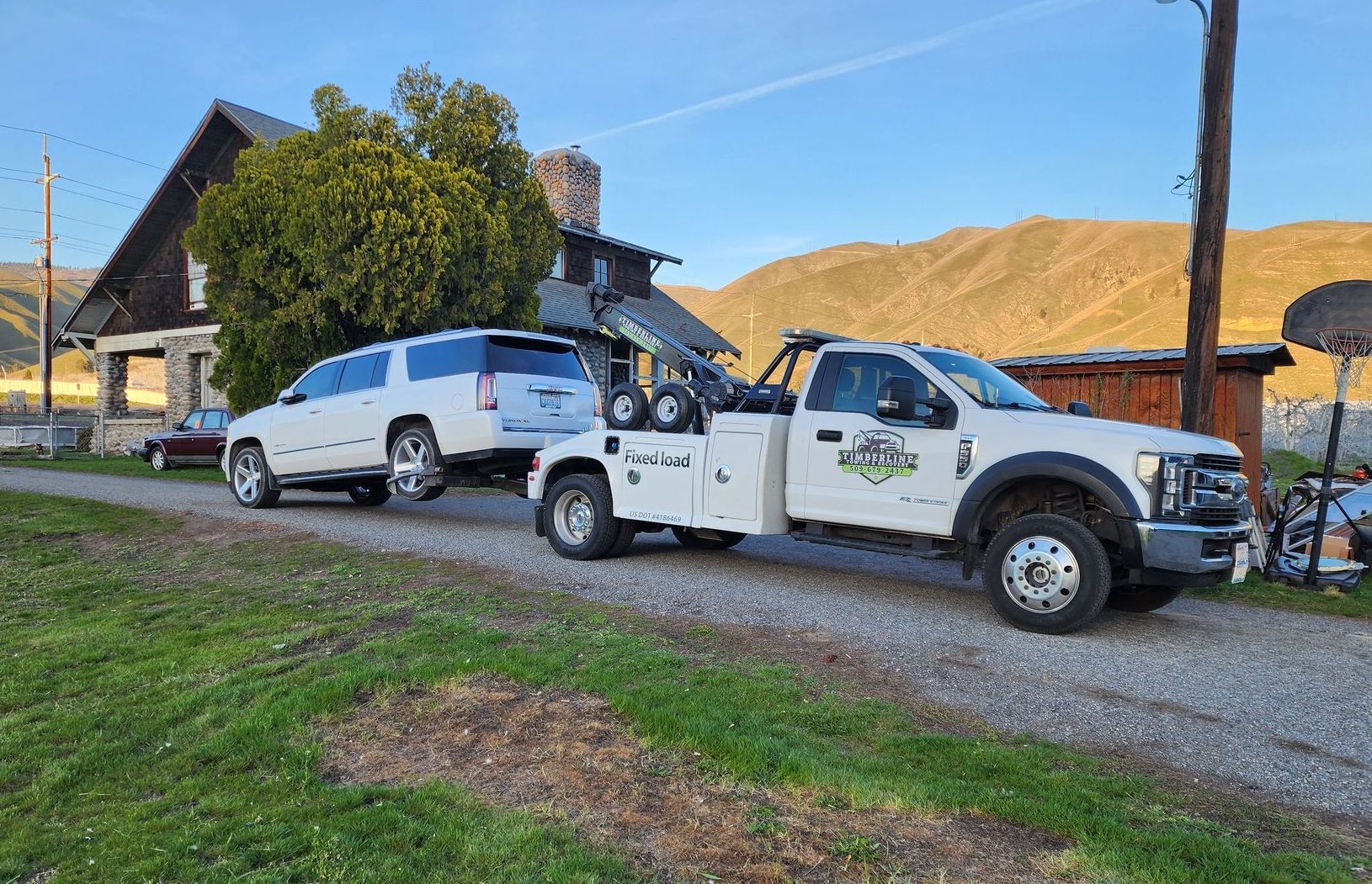 A white tow truck is towing a white suv down a gravel road.