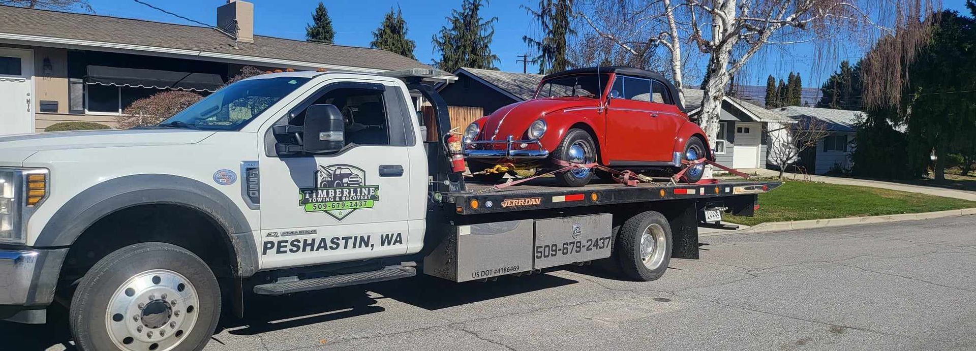 A tow truck with a red car on the back is parked in front of a house.