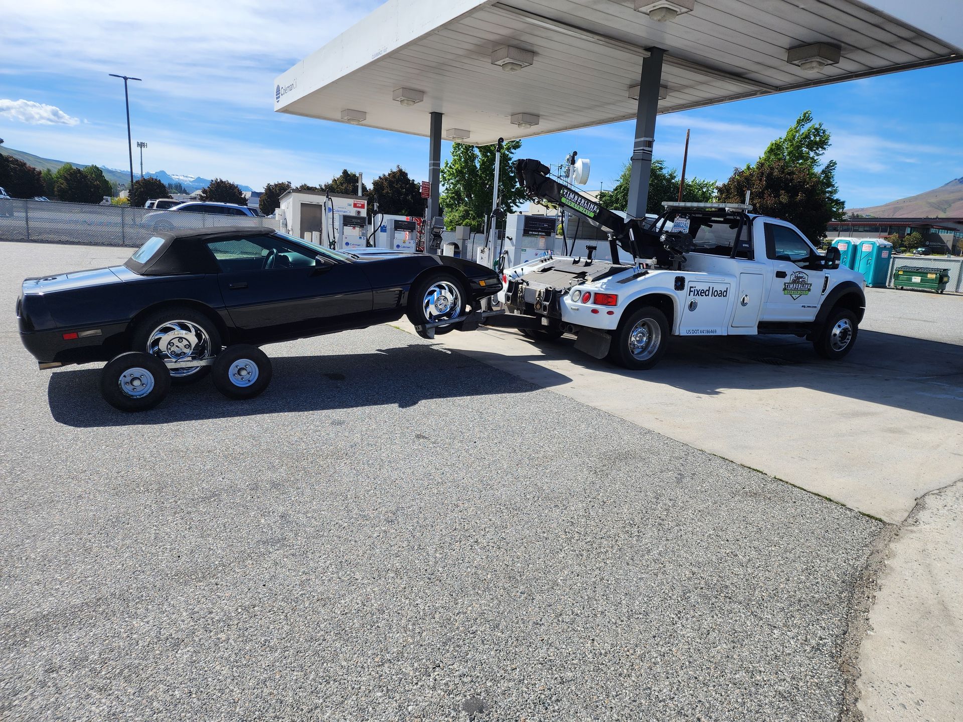 A tow truck is towing a black car in a parking lot.