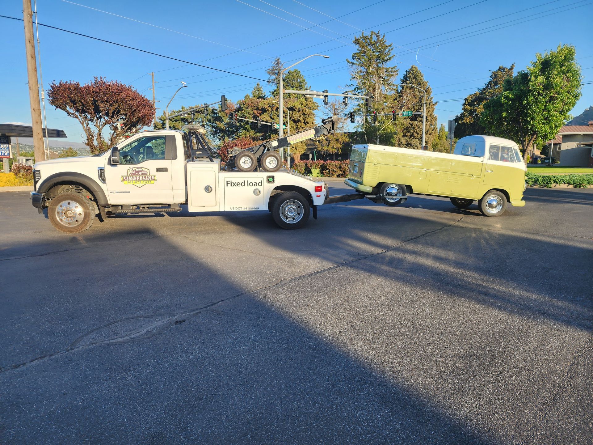A white tow truck is towing a green van down a street.