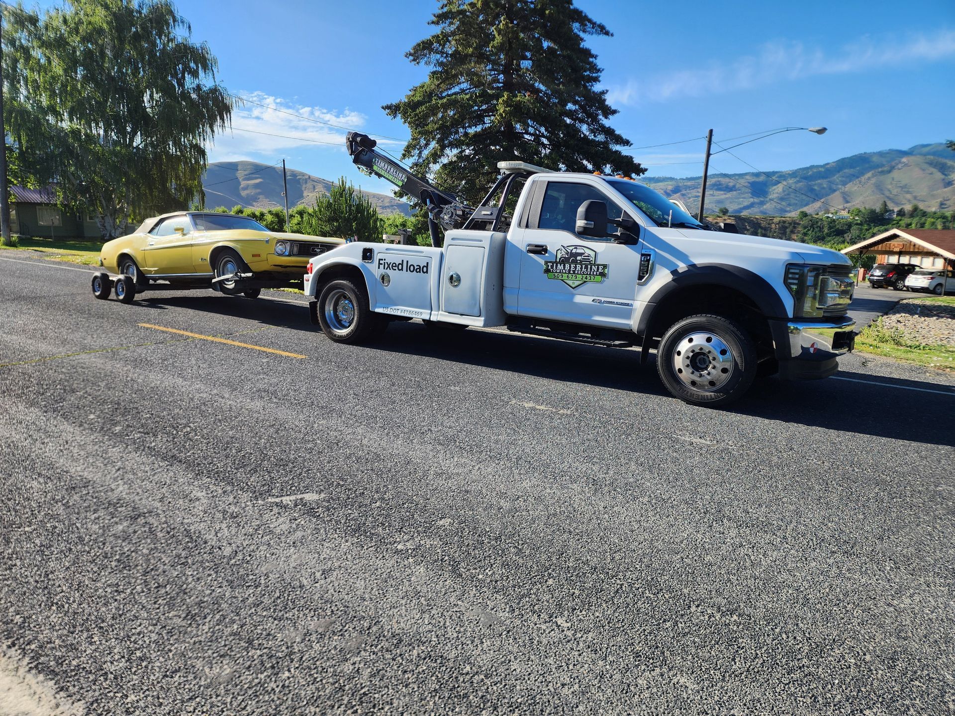 A tow truck is towing a yellow car down a road.