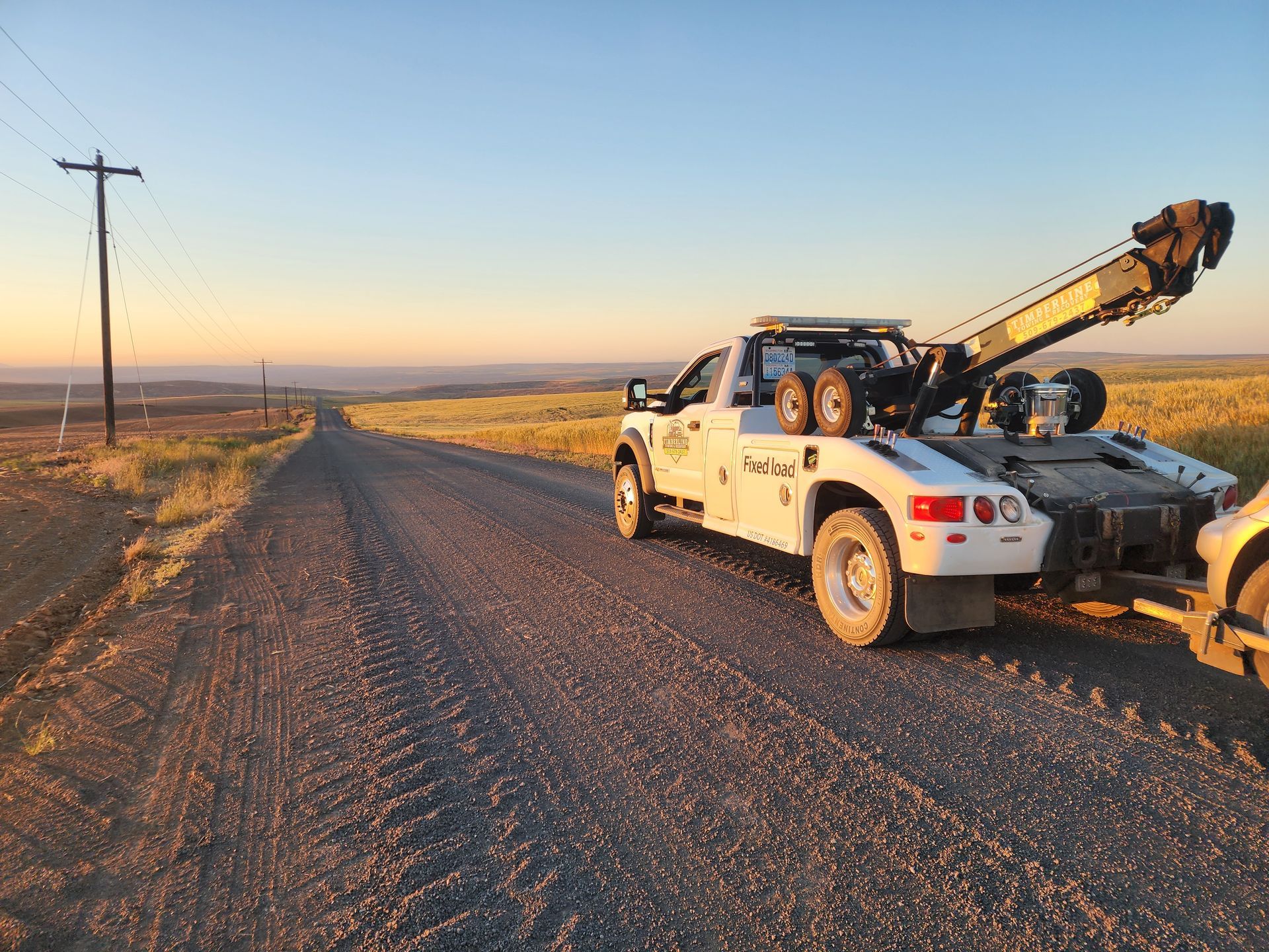 A tow truck is towing a car down a dirt road.