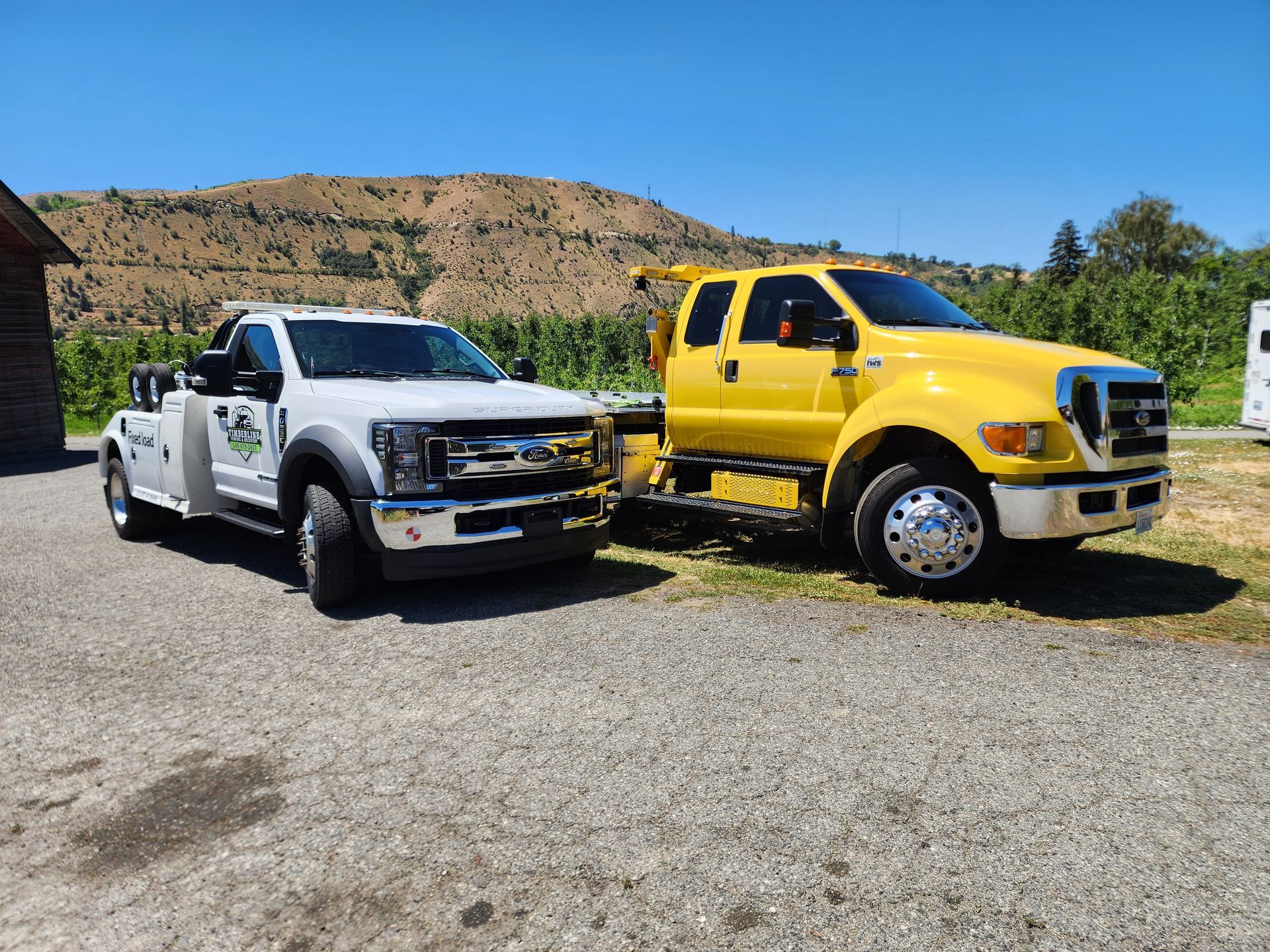 Two tow trucks are parked next to each other on a gravel road.
