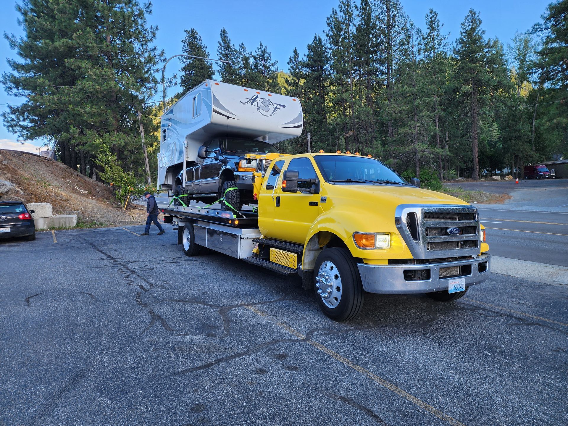 A yellow tow truck is carrying a rv down a road.