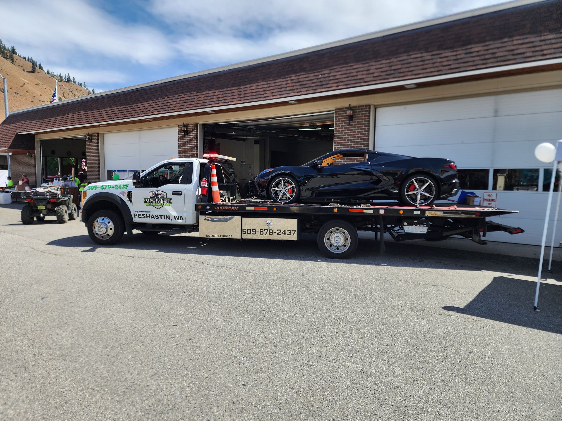 A tow truck with a black sports car on the back is parked in front of a garage.