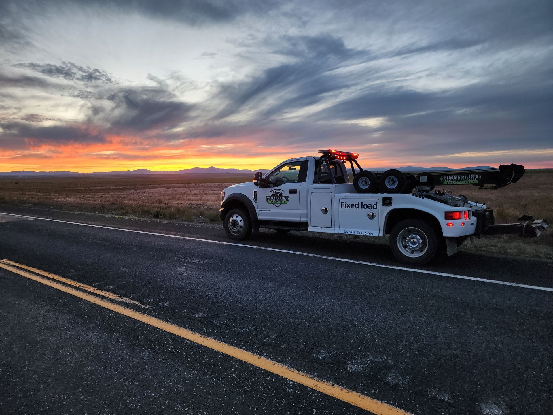 A white tow truck is parked on the side of the road at sunset.