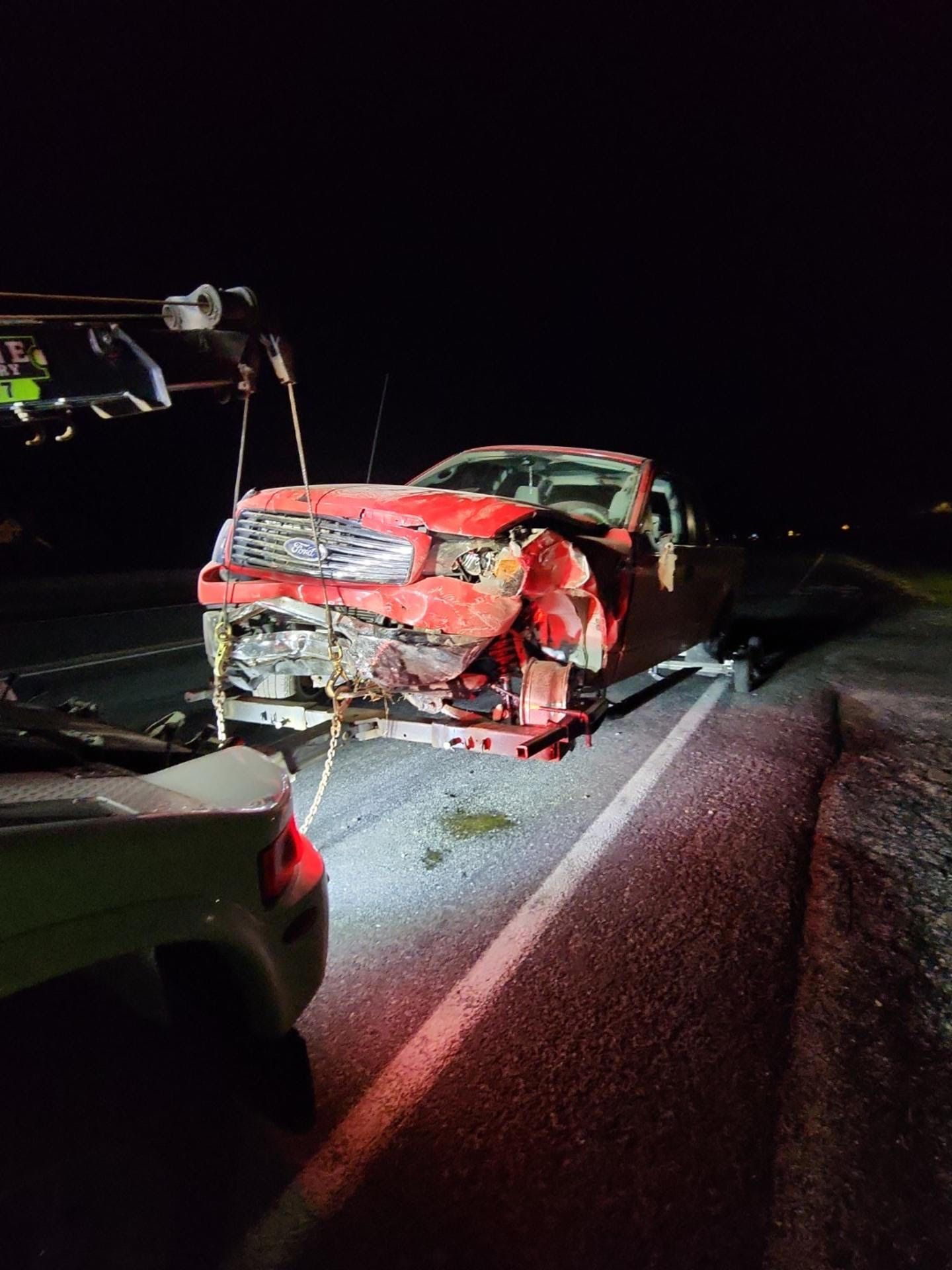 A red truck is being towed down a road at night.