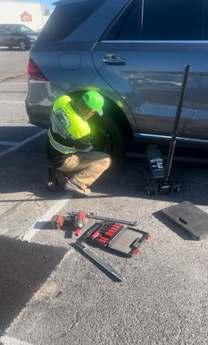 A man is kneeling down next to a car in a parking lot.