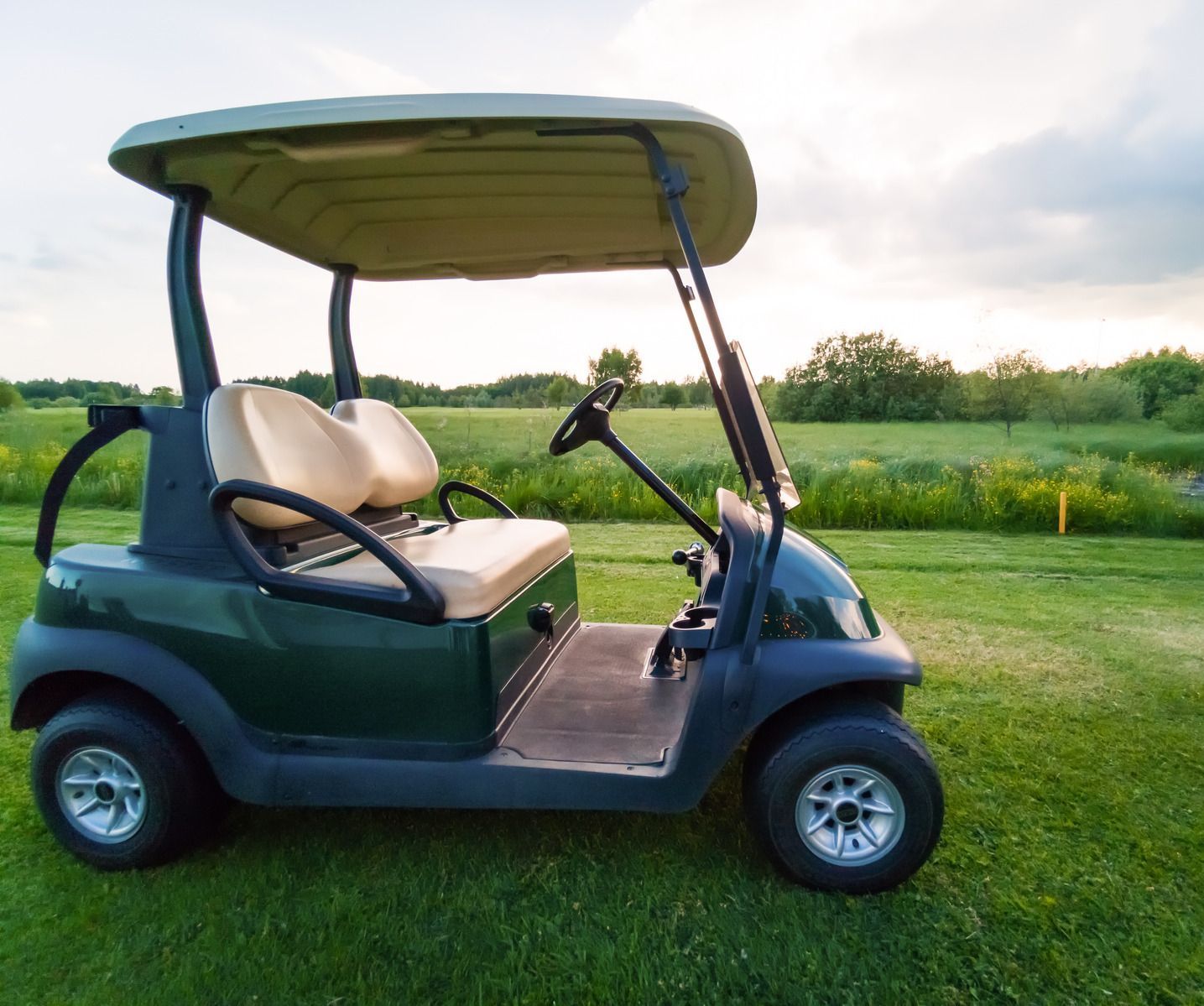 A green golf cart is parked in a grassy field