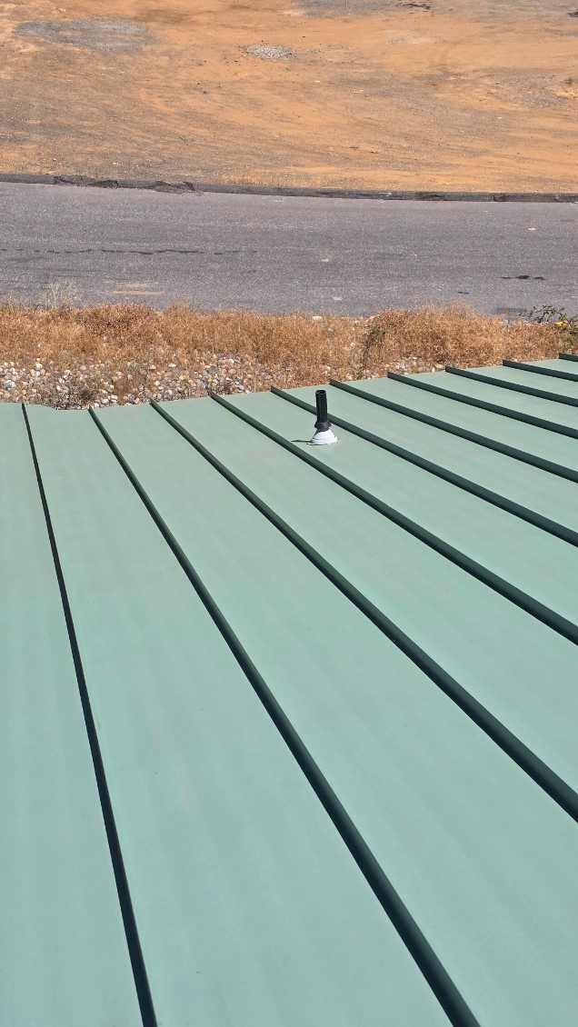Green metal roof with a pipe extending up, against a brown and gray background.
