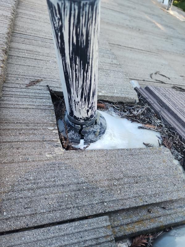 Close-up of a roof vent pipe sealed with white caulk, with cracked asphalt shingles surrounding it.