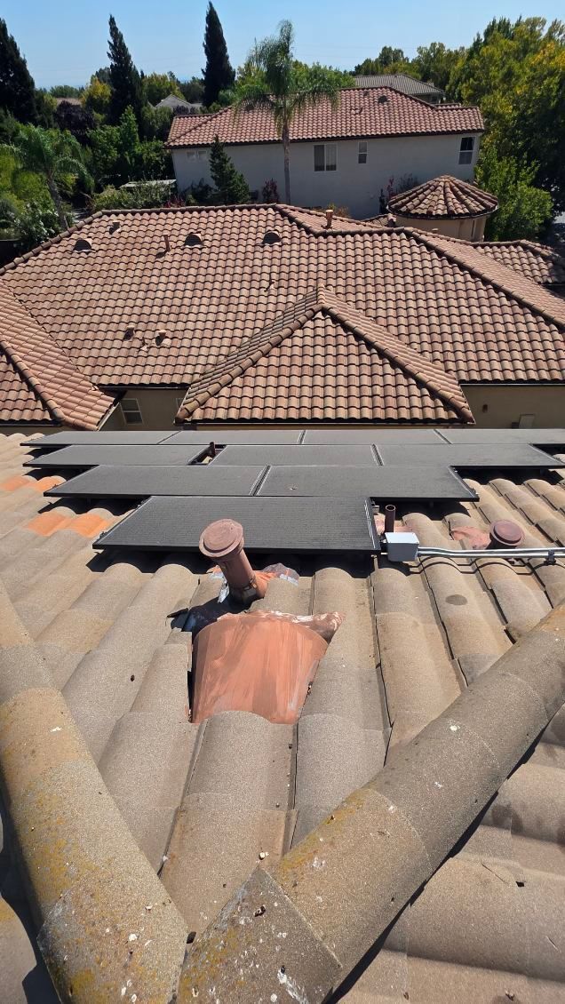 Terracotta tiled roof with solar panels; houses in background under a sunny sky.