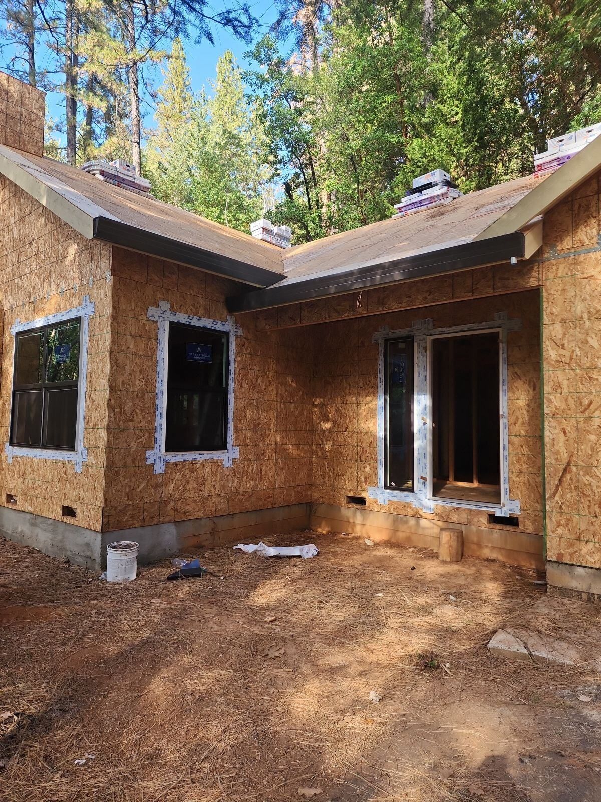 House under construction; wood siding, windows, and roof in a forest setting.