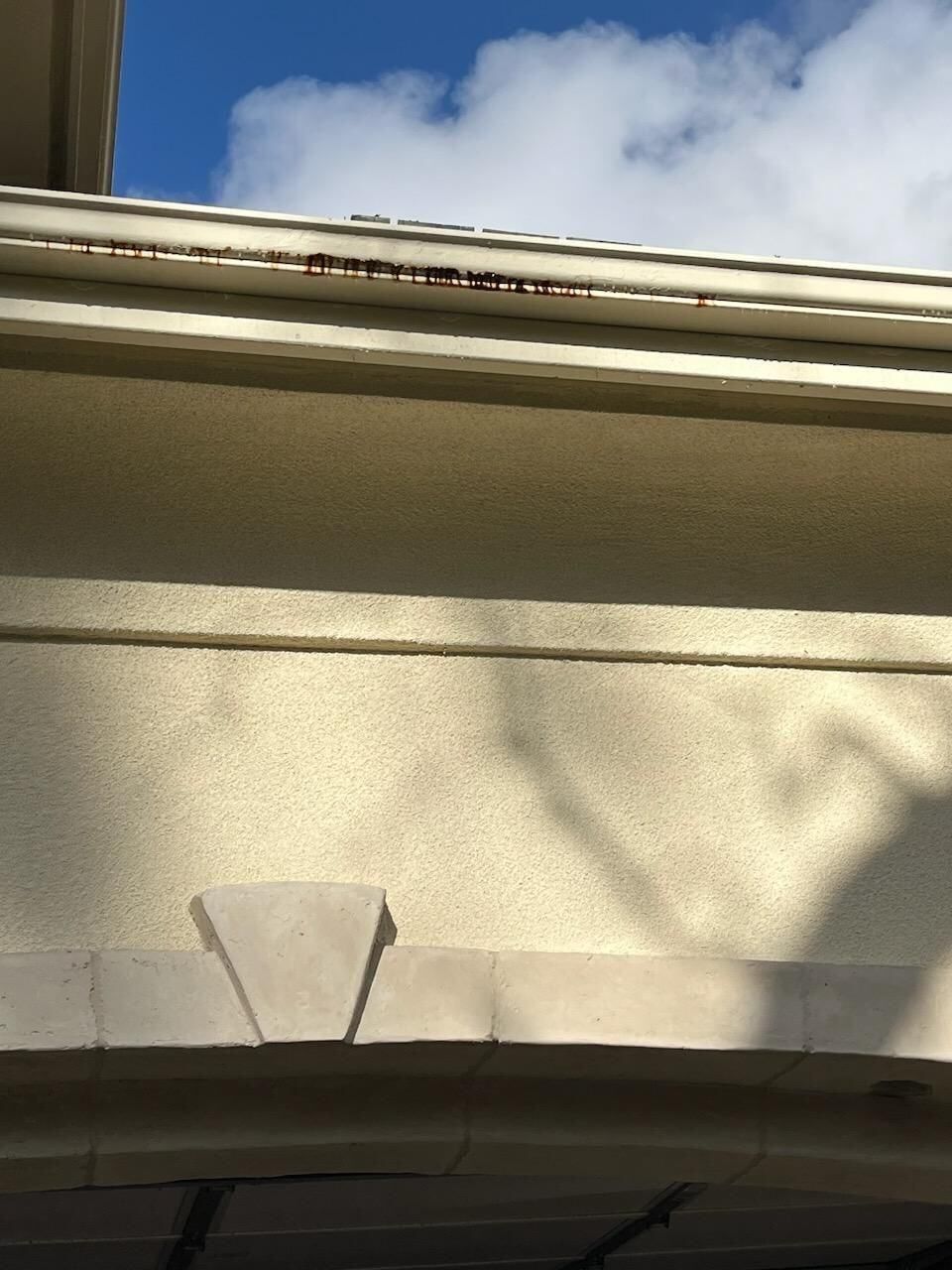 Beige stucco wall with a dark brown gutter against a cloudy blue sky.