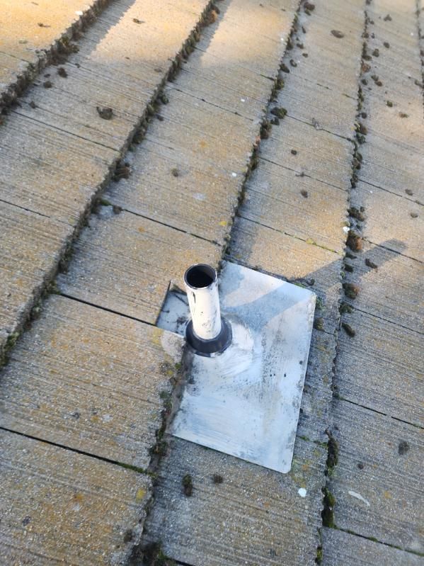 Roof vent pipe protruding from a weathered roof with concrete tiles, surrounded by debris.