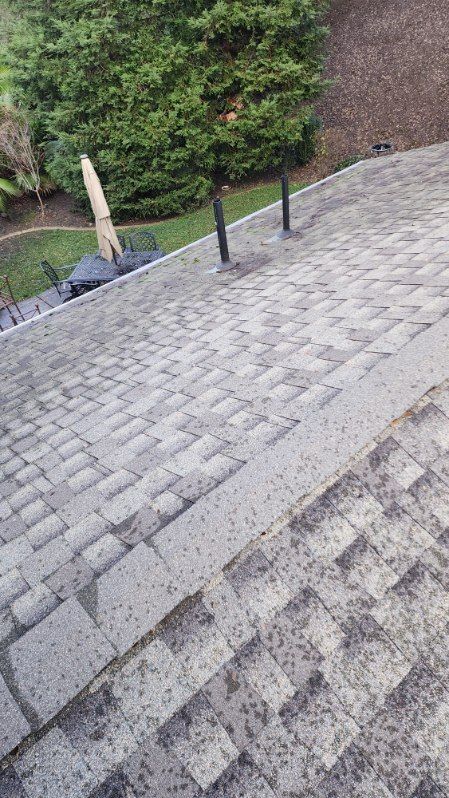 Gray asphalt shingle roof with two black pipes extending upwards.