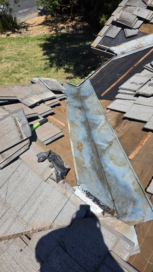 Rooftop with torn shingles and damaged metal flashing. A shadow of a person is visible.