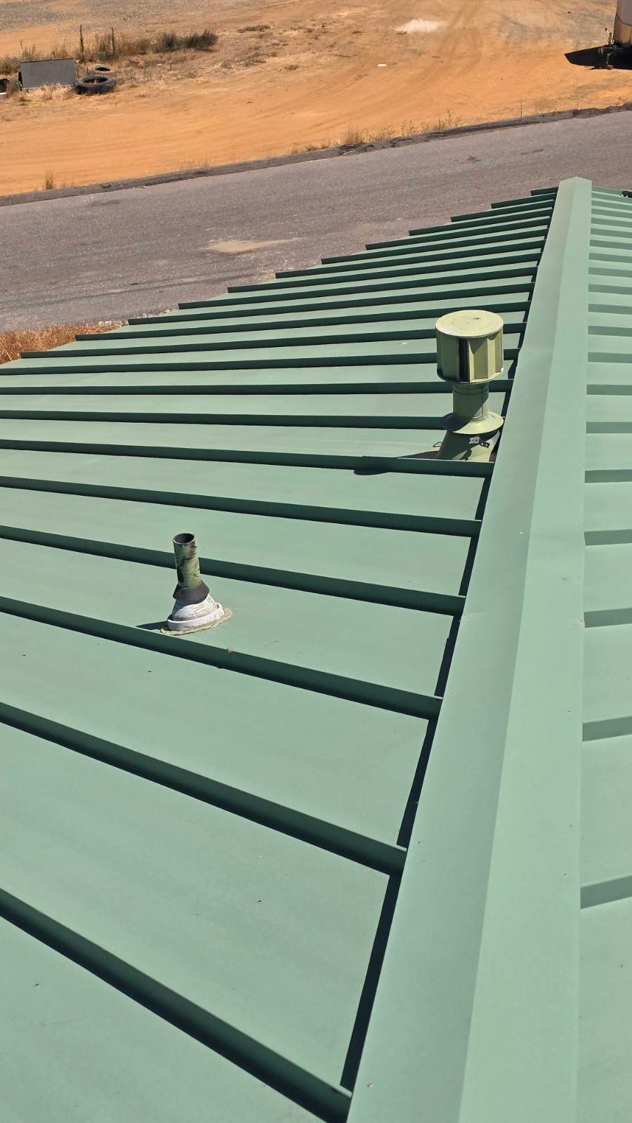 Green metal roof with two vents; angled view on a sunny day.
