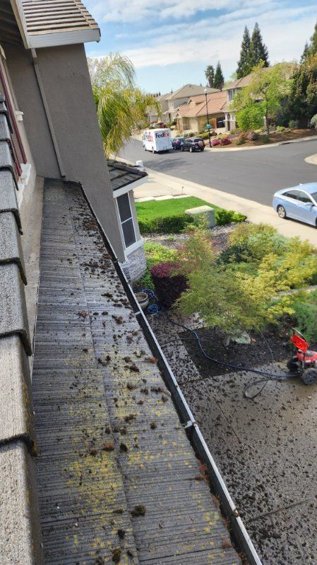View of a house gutter filled with debris; neighborhood street and landscaping in the background.